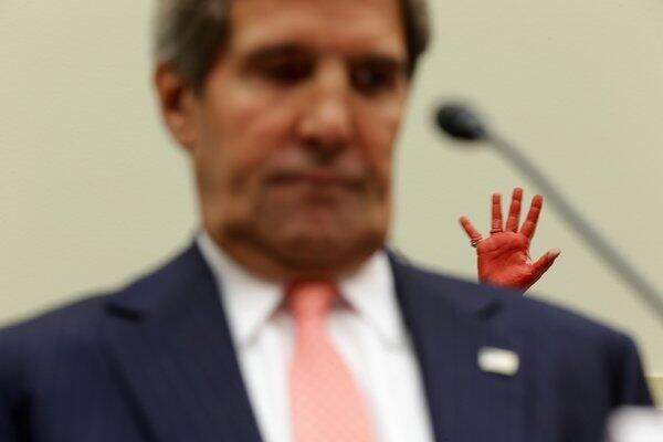 A protester holds up her hand, covered in red paint symbolizing blood, as Secretary of State John F. Kerry testifies Wednesday during a House hearing on proposed military strikes against Syria.