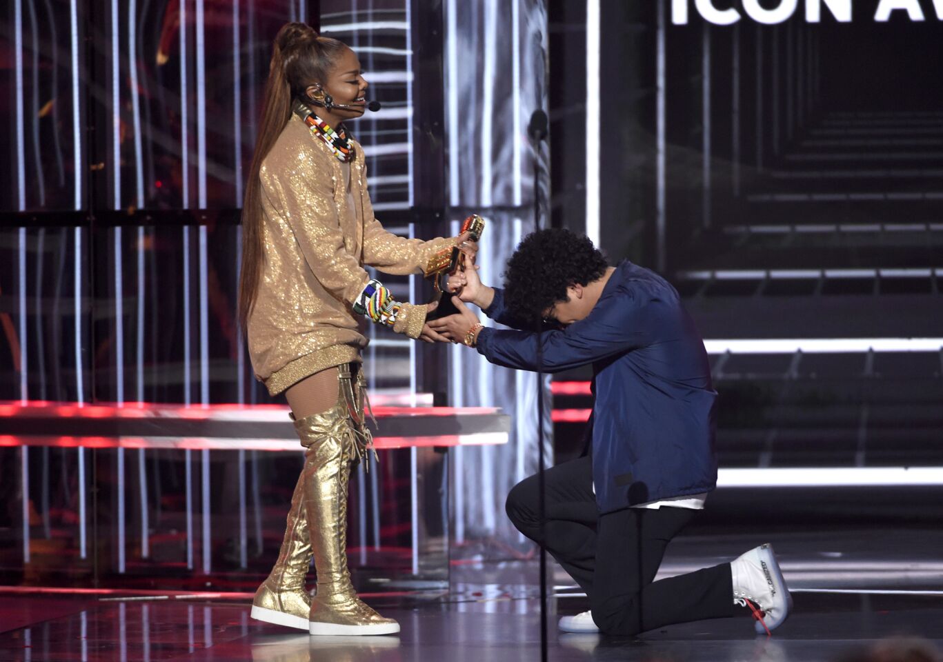 Bruno Mars kneels to present the Icon Award to Janet Jackson.
