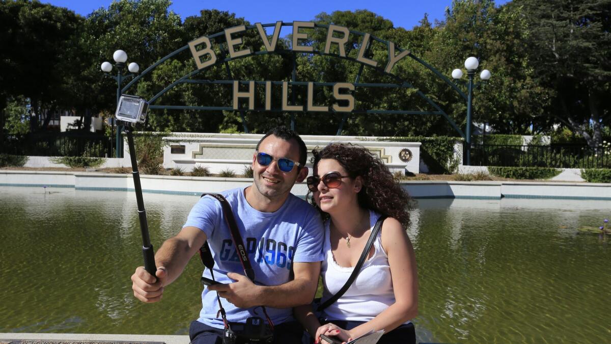 Sevag and Houry Alsanian, tourists from Lebanon, take photos in front of the Beverly Hills sign in Beverly Gardens Park on Oct. 30, 2015. The Beverly Hills Conference & Visitors Bureau is proposing a tour bus stop in the city's business district.