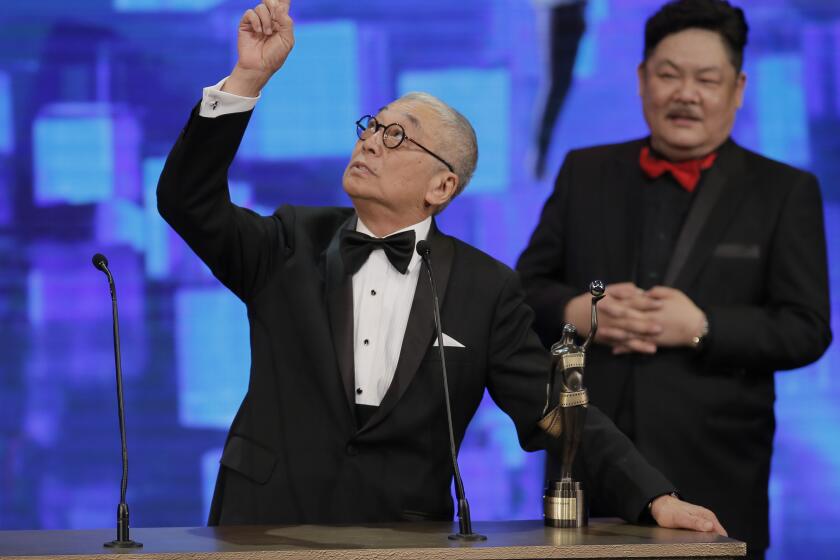 A man in a tuxedo standing behind a podium and pointing up to the sky