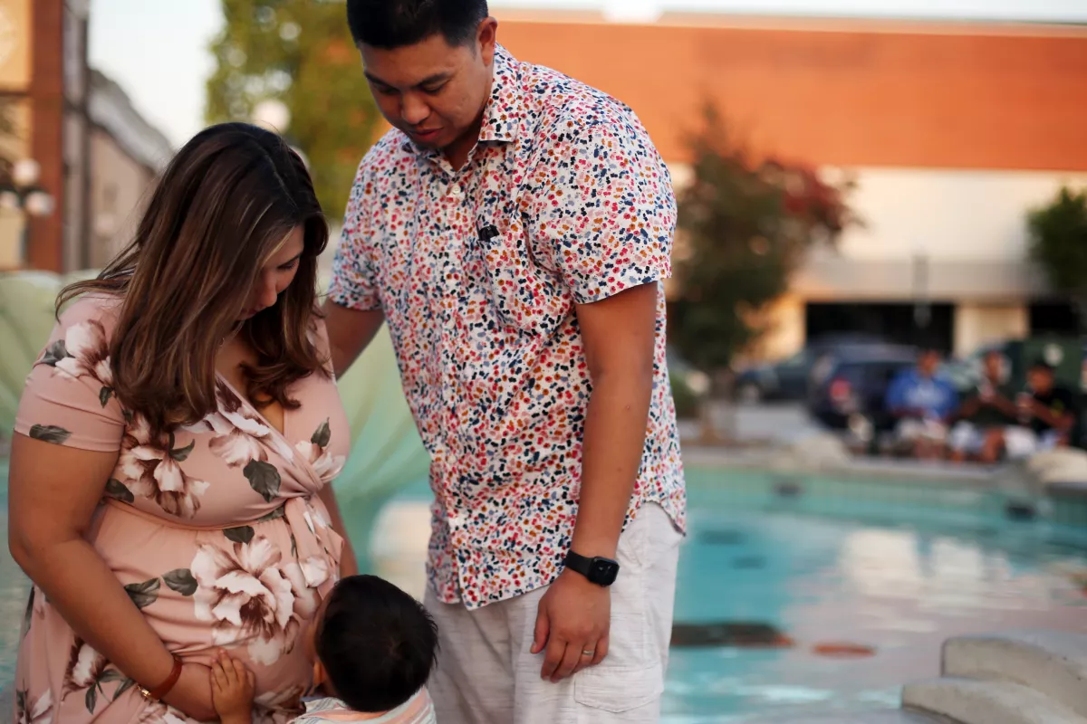 A pregnant woman, a man and a little boy stand together outside.