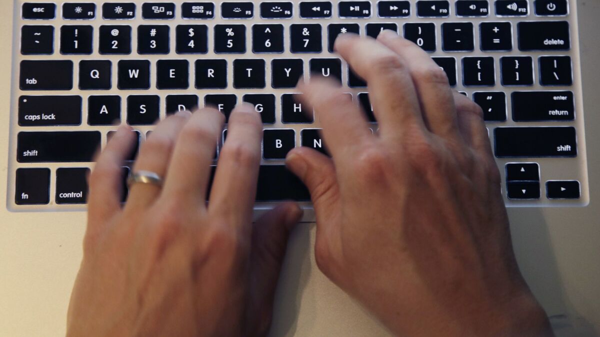 Fingers type on a laptop keyboard.