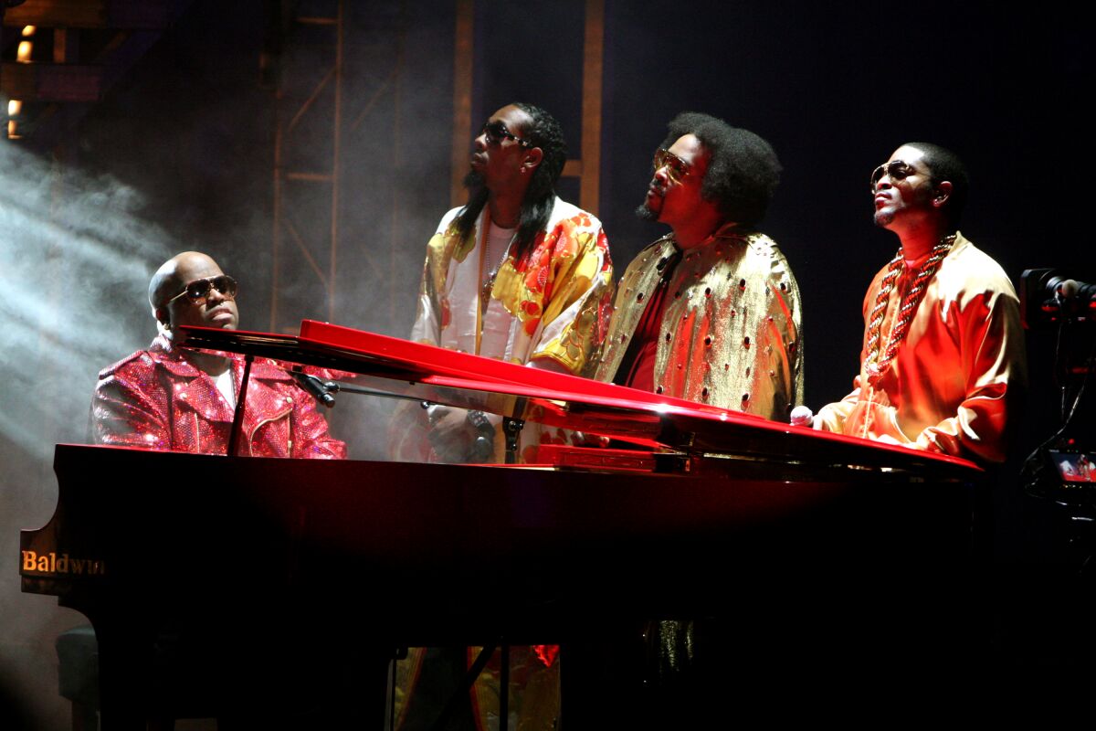 Three men sing while one, left, plays the piano.