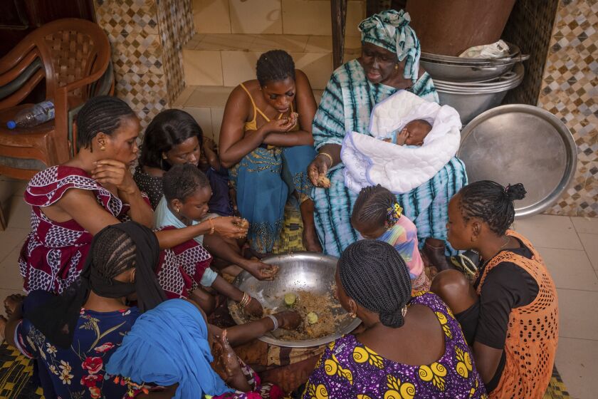 La familia Fall se reúne para compartir la comida, un gran tazón de thieboudienne _el platillo nacional de Senegal_, el 31 de mayo de 2022, en Diamniadio, Senegal. (AP Foto/Grace Ekpu)