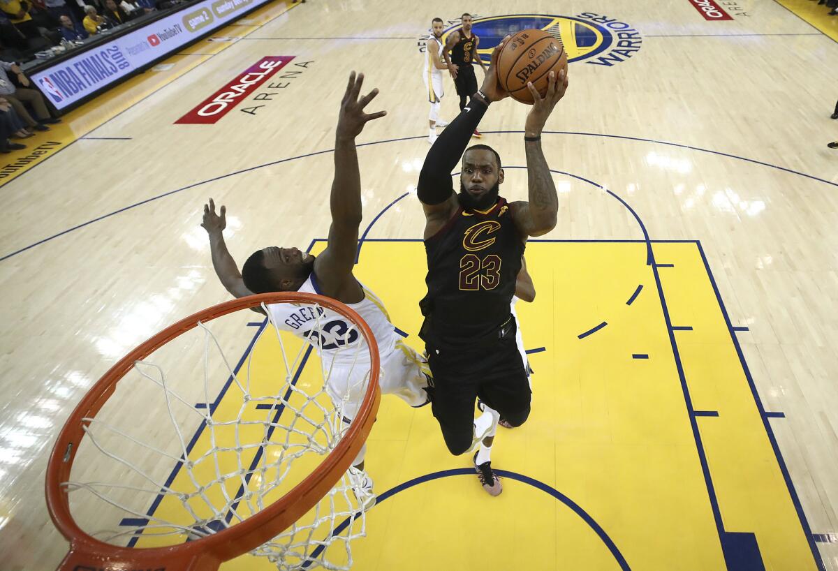 LeBron James, derecha, de los Cavaliers de Cleveland, se eleva para enfestar ante Draymond Green, de los Warriors de Golden State, en el primer partido de la final de la NBA en Oakland, California, el jueves 31 de mayo de 2018. Los Warriors ganaron 124-114 en tiempo extra.