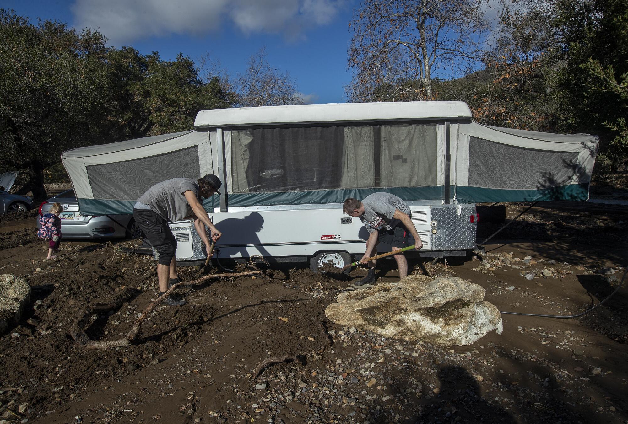 Klint Gardiner, left, helps Jantzen Allphin remove mud and debris from underneath Allphin's pop-up trailer 
