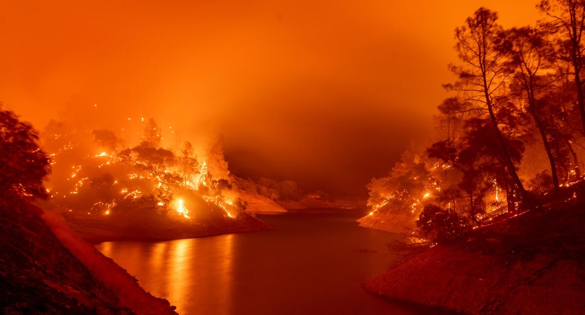 Flames burn on both sides of Lake Berryessa, casting the air in a ghostly orange shroud