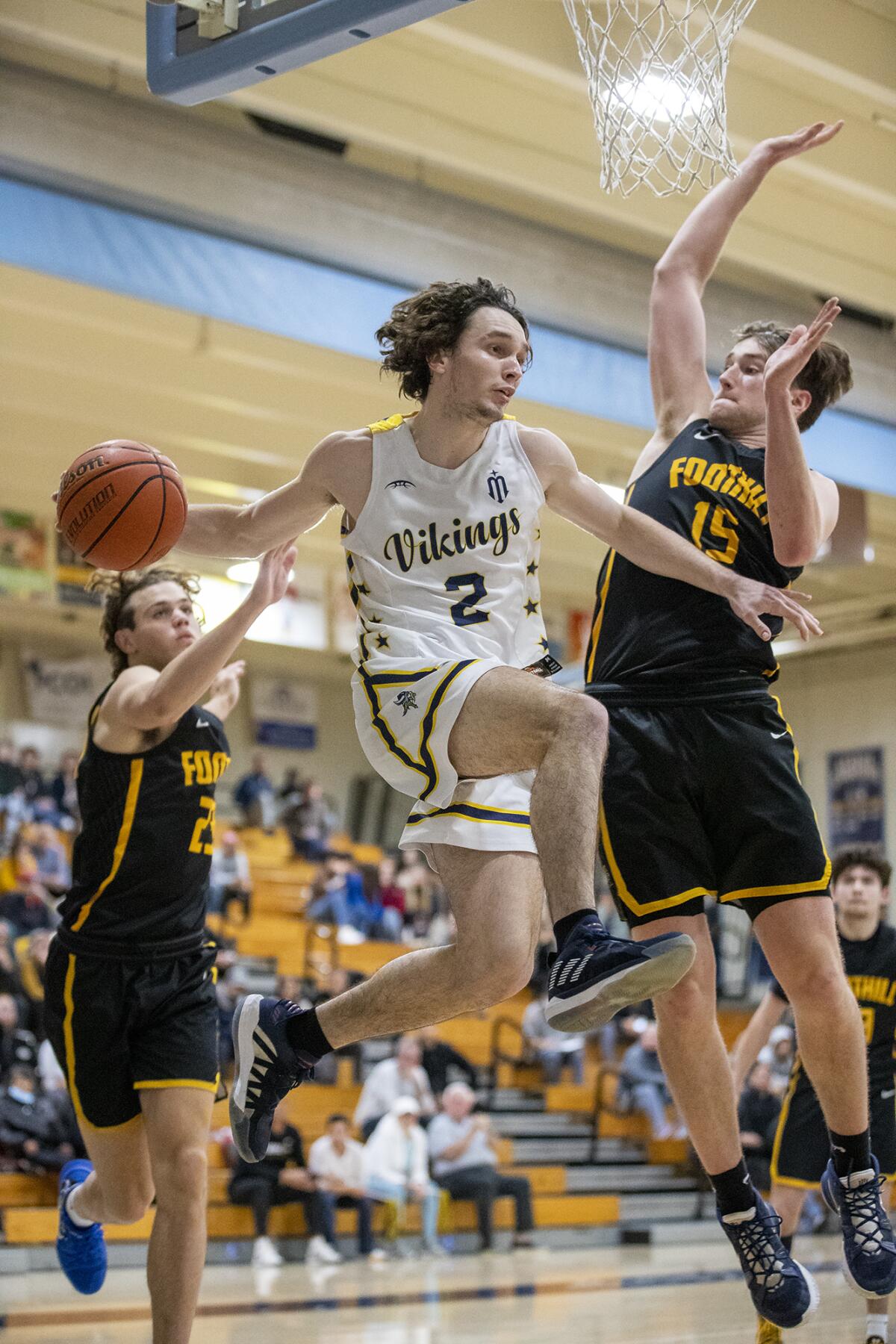 Marina's Eric Hodgkins looks to pass the ball under the hoop under pressure from Foothill's Braedyn Benhard.