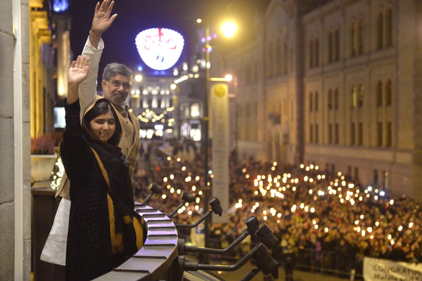 Nobel Peace Prize laureates Malala Yousafzai and Kailash Satyarthi wave from the balcony of Grand Hotel during a torchlight procession in their honor in Oslo, Norway, 2014.