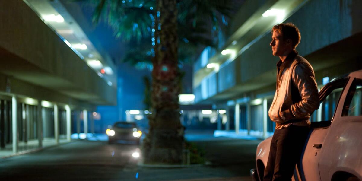 A guy in a cool jacket leans against a muscle car in the light-polluted Los Angeles night