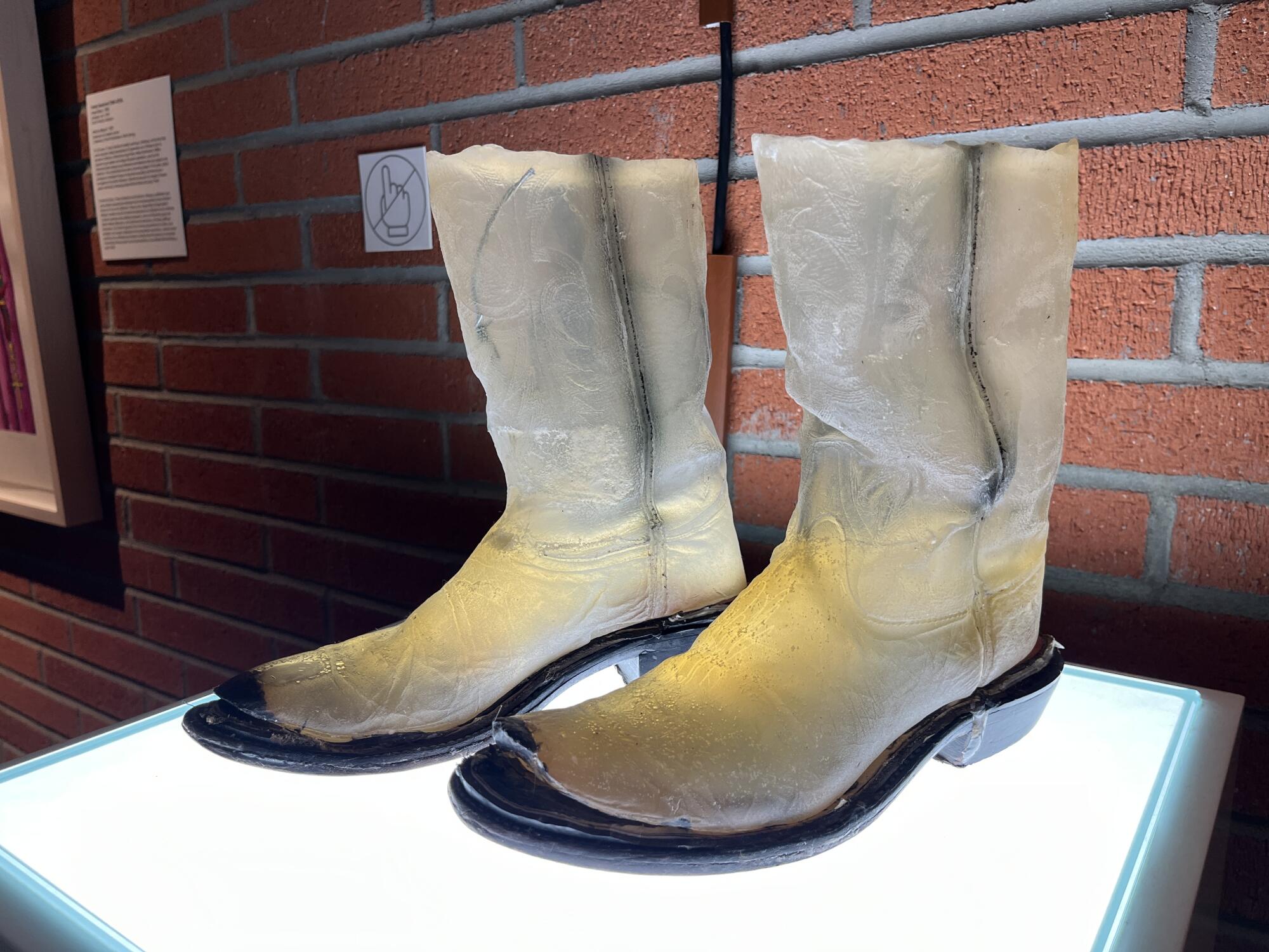 A pair of translucent boots made out of melted soaps stand atop an illuminated plinth.
