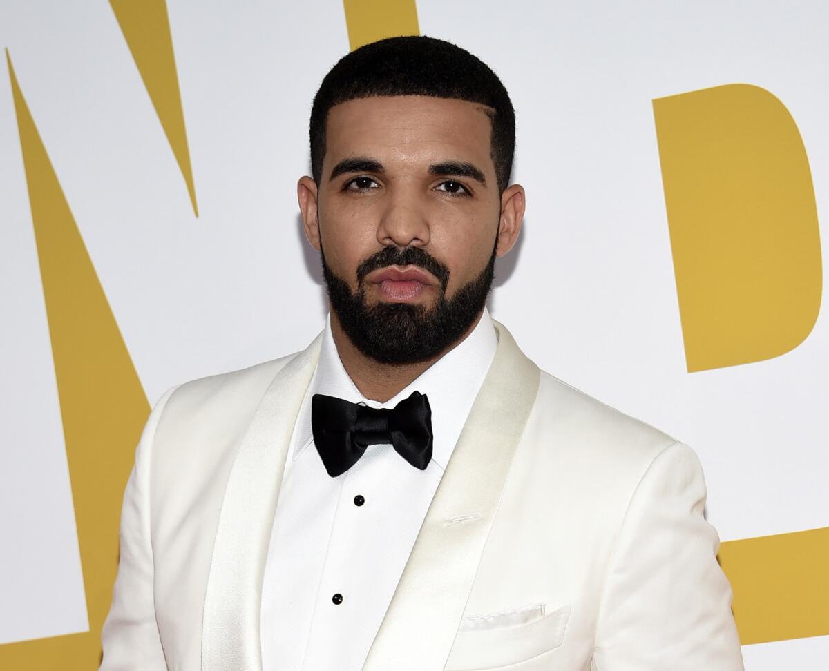 Drake wearing a white tuxedo jacket and shirt and a black bow tie as he poses with a straight face