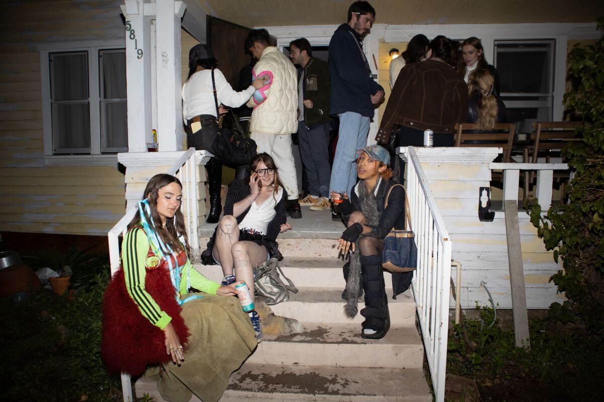 A group of people stand and sit on a house's porch and steps.