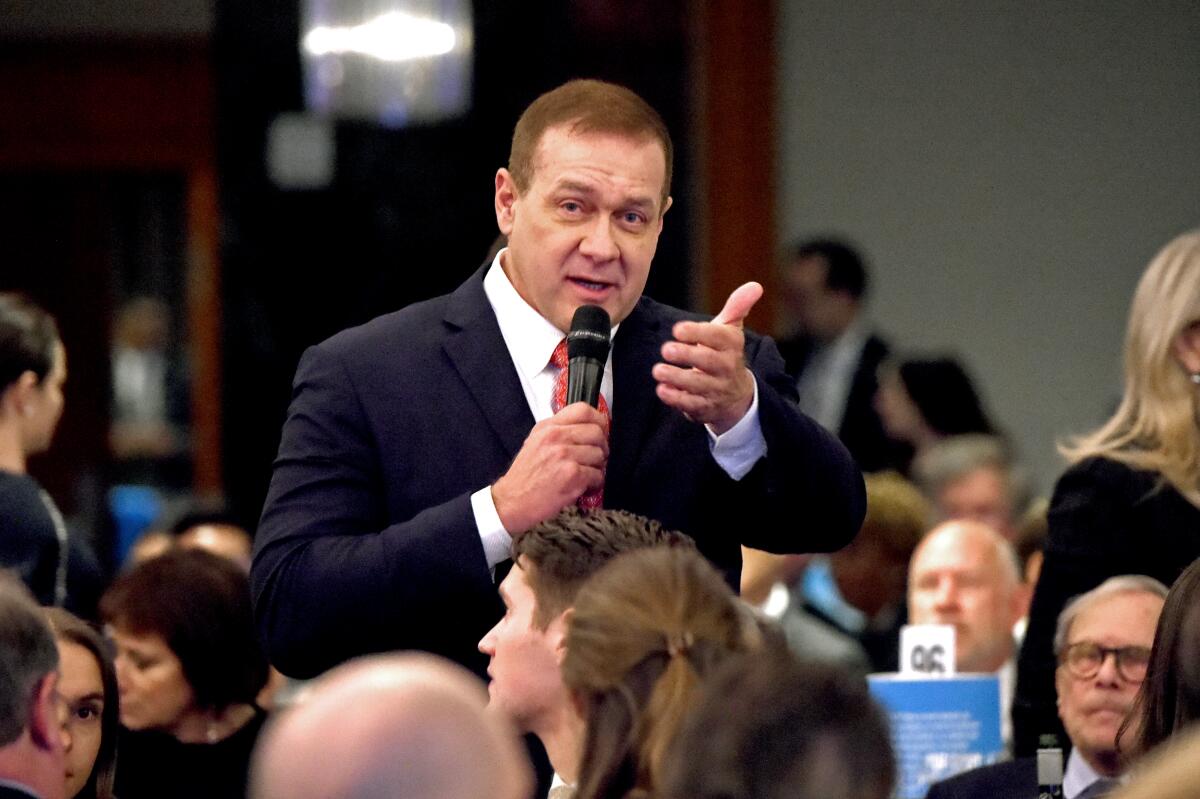 Scott Minerd, standing amid a seated crowd, speaks into a microphone at a 2018 event.