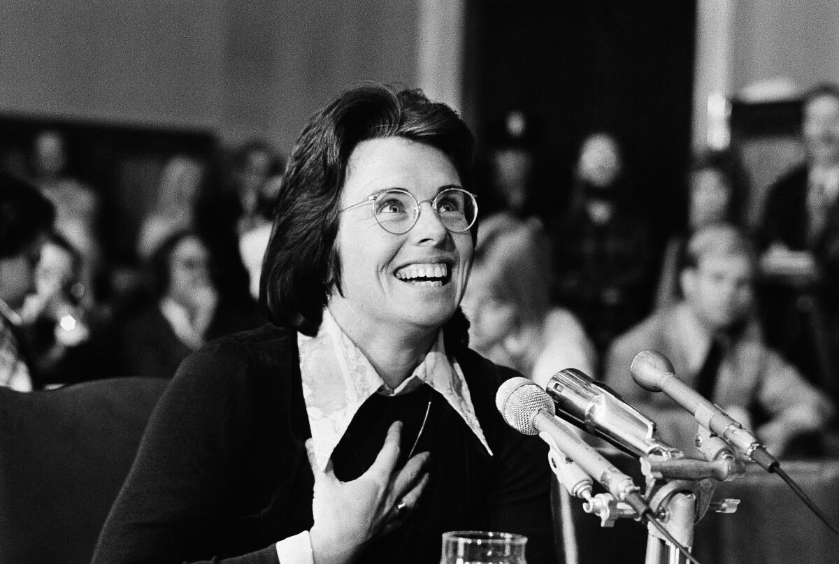 Commentary: She left faculty to overcome tennis. At 81, Billie Jean King is again, chasing a level 3 A woman with dark hair and glasses smiles while speaking before mics
