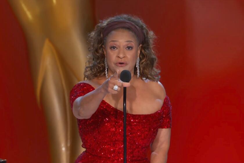A woman in a sparkly red dress speaking into a microphone and pointing