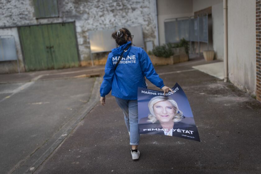 FILE - Emma Mino holds an electoral poster of French far-right presidential candidate Marine Le Pen, Tuesday, March 29, 2022 in Le Temple-De-Bretagne, western France. Marine Le Pen’s vision for France if the far-right leader wins Sunday’s runoff presidential election would include a ban on Muslim headscarves in public, schoolchildren in uniforms and laws passed by referendum. (AP Photo/Jeremias Gonzalez, File)