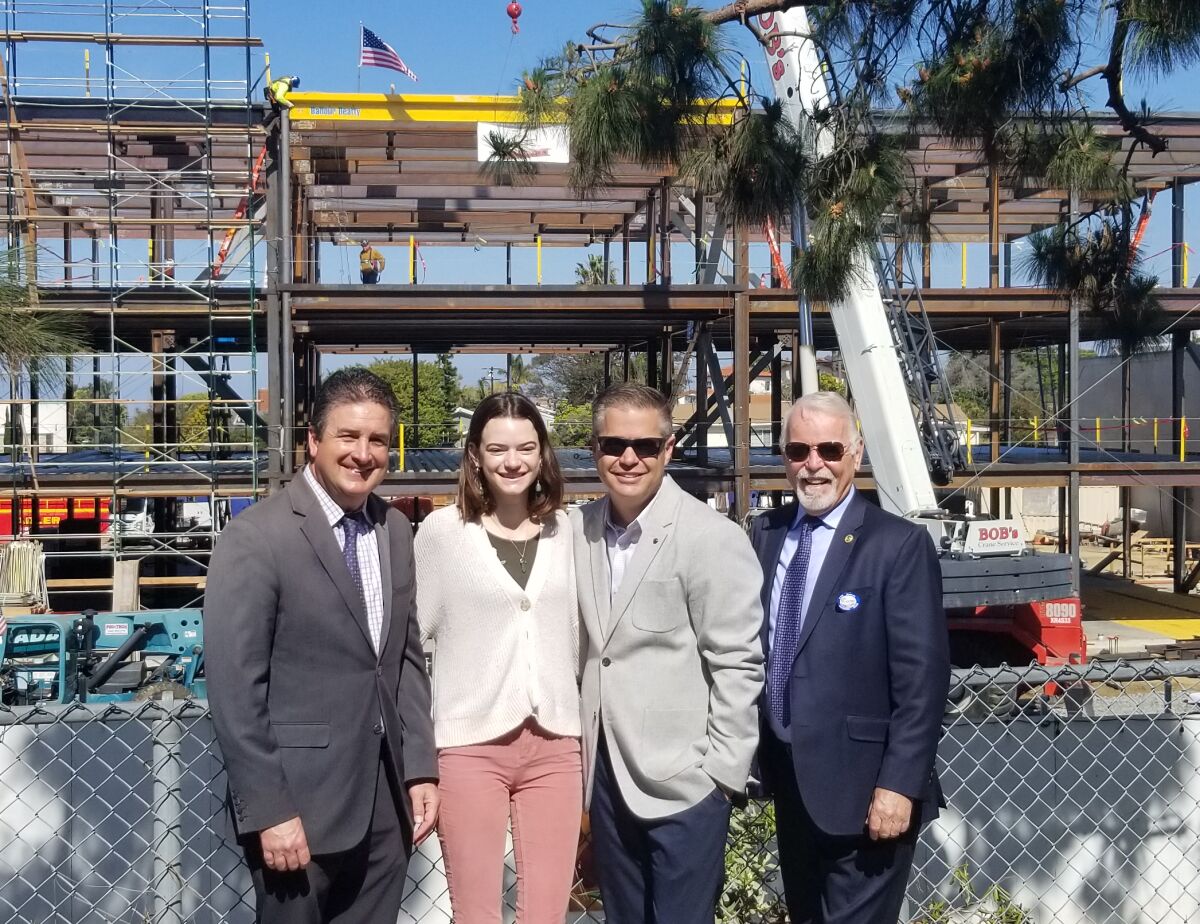 Lee Dulgeroff (chief facilities planning and construction officer), Ila Komasa (Point Loma High School ASB president and a senior), principal Hans Becker and Michael McQuary (a San Diego Unified Board of Education trustee) commemorate a construction milestone for the new, three-story 800 Building; as the final beam — painted gold in support of PLHS colors (maroon and gold) — is lowered into place.