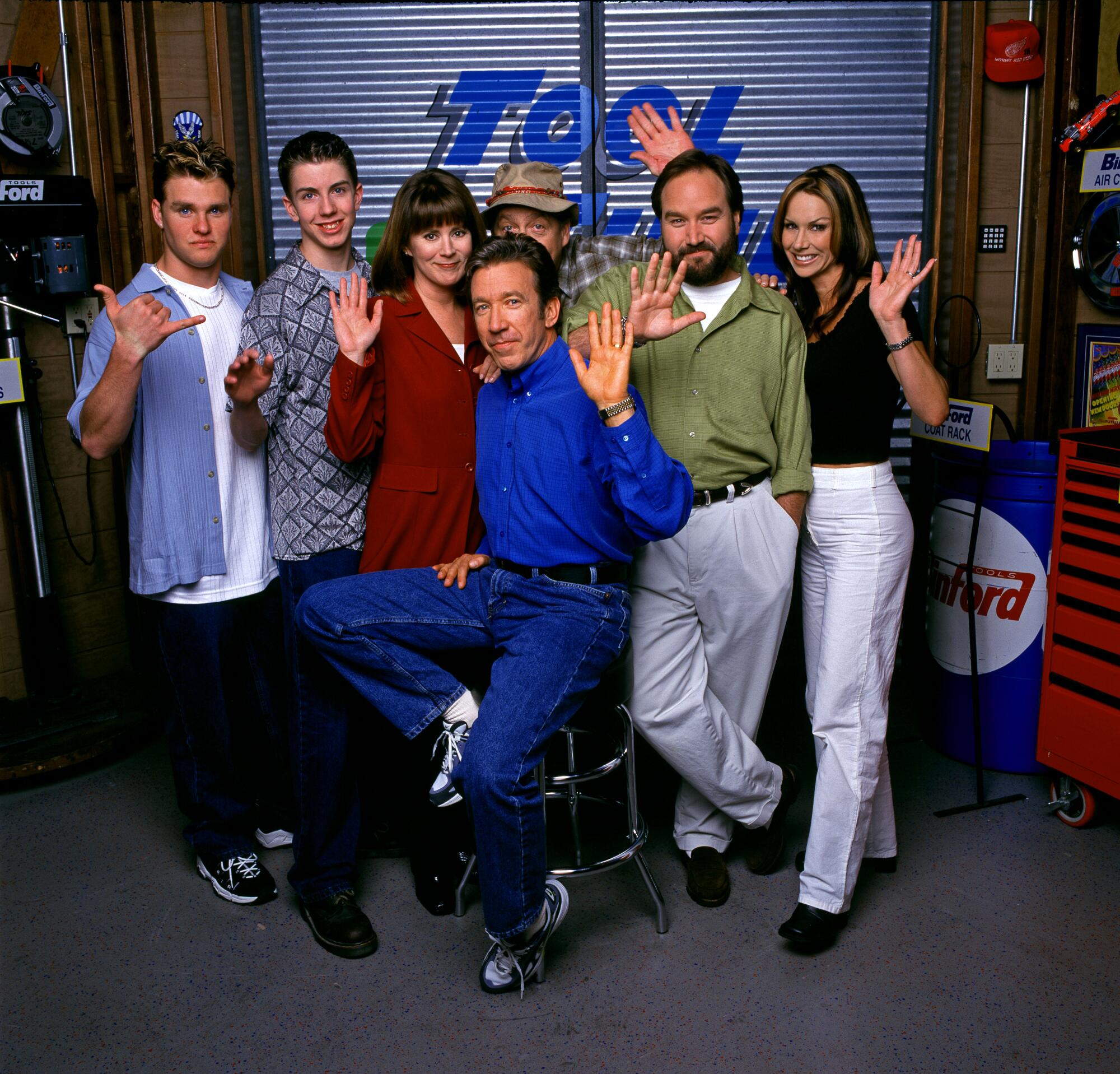 A group of actors waving in front of a metal garage gate.