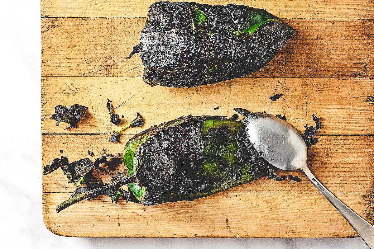A spoon is used to scrape off the charred skin from the roasted poblano peppers.  