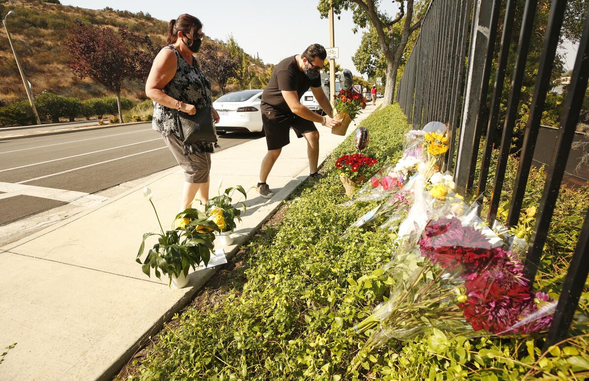 People place flowers along a metal fence with other flowers.