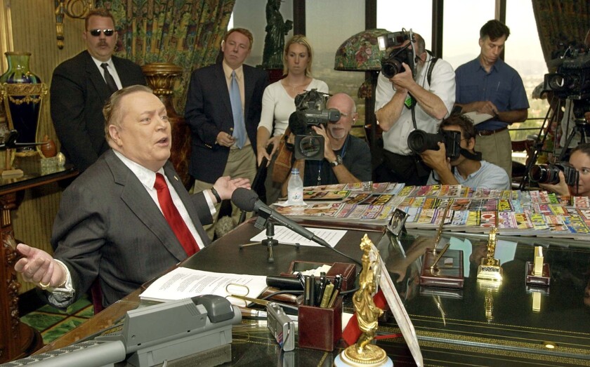 Larry Flynt speaks into a microphone with reporters and photographers nearby in 2003.