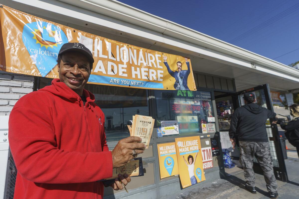 A smiling man standing in front of a convenience store holds several lottery tickets.