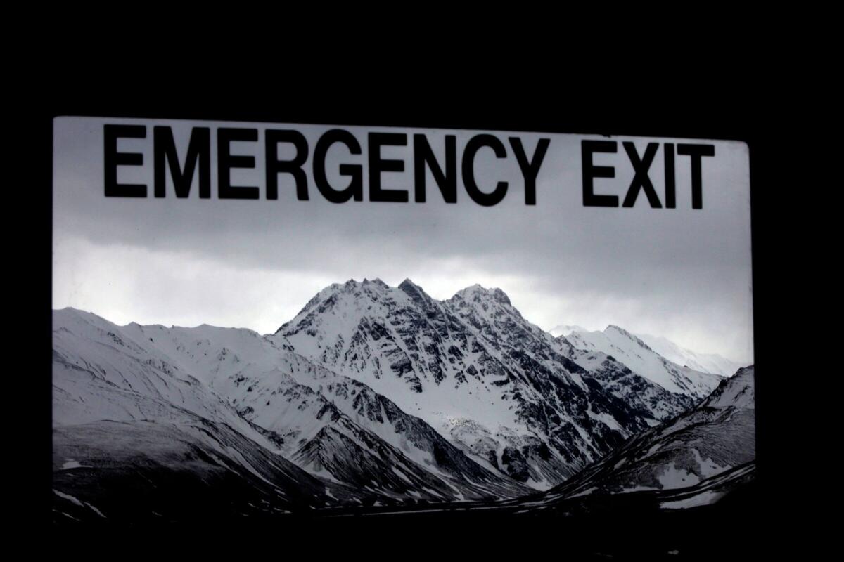 Mountains loom beyond a tour bus window's exit sign in Alaska's Denali National Park.