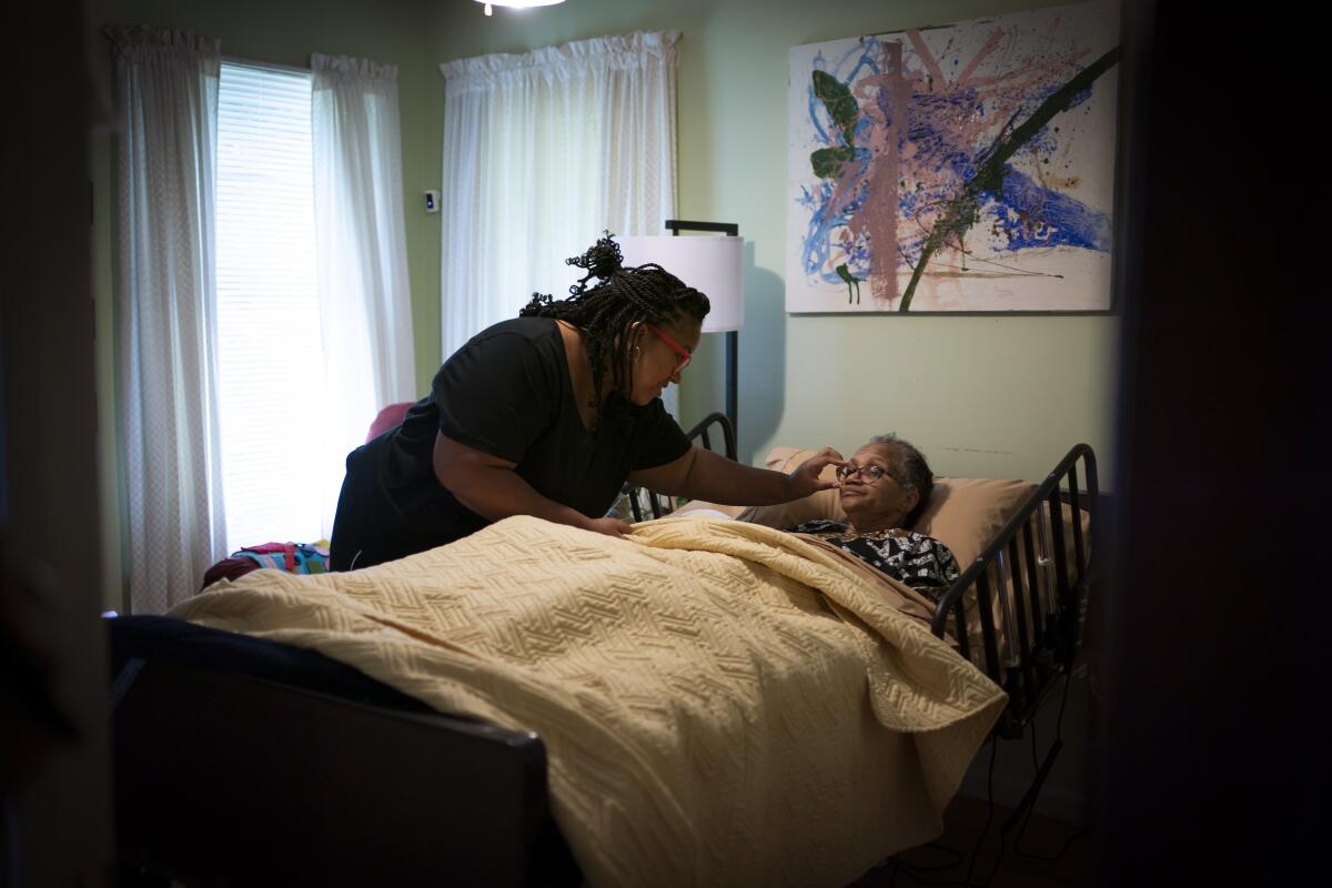 A woman leaning over an older woman in a hospital-style bed, adjusting her glasses.