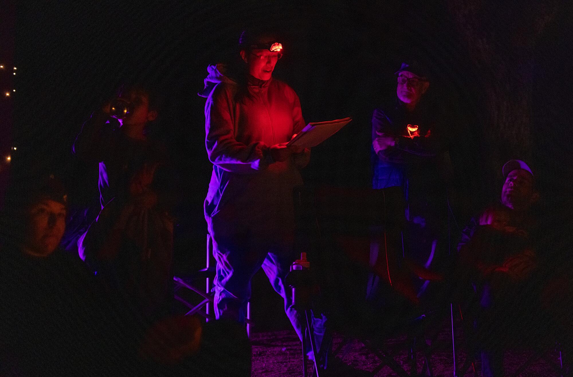  Dani Hsia, center, a headlamp illuminating her handwritten notes, speaks to a group sitting around a campfire. 