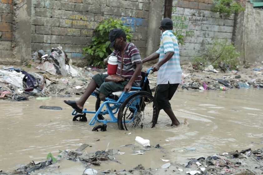 Un hombre en silla de ruedas recibe ayuda para cruzar una calle inundada por fuertes lluvias, el sábado 3 de junio de 2023, en Puerto Príncipe, Haití. (AP Foto/Odelyn Joseph)