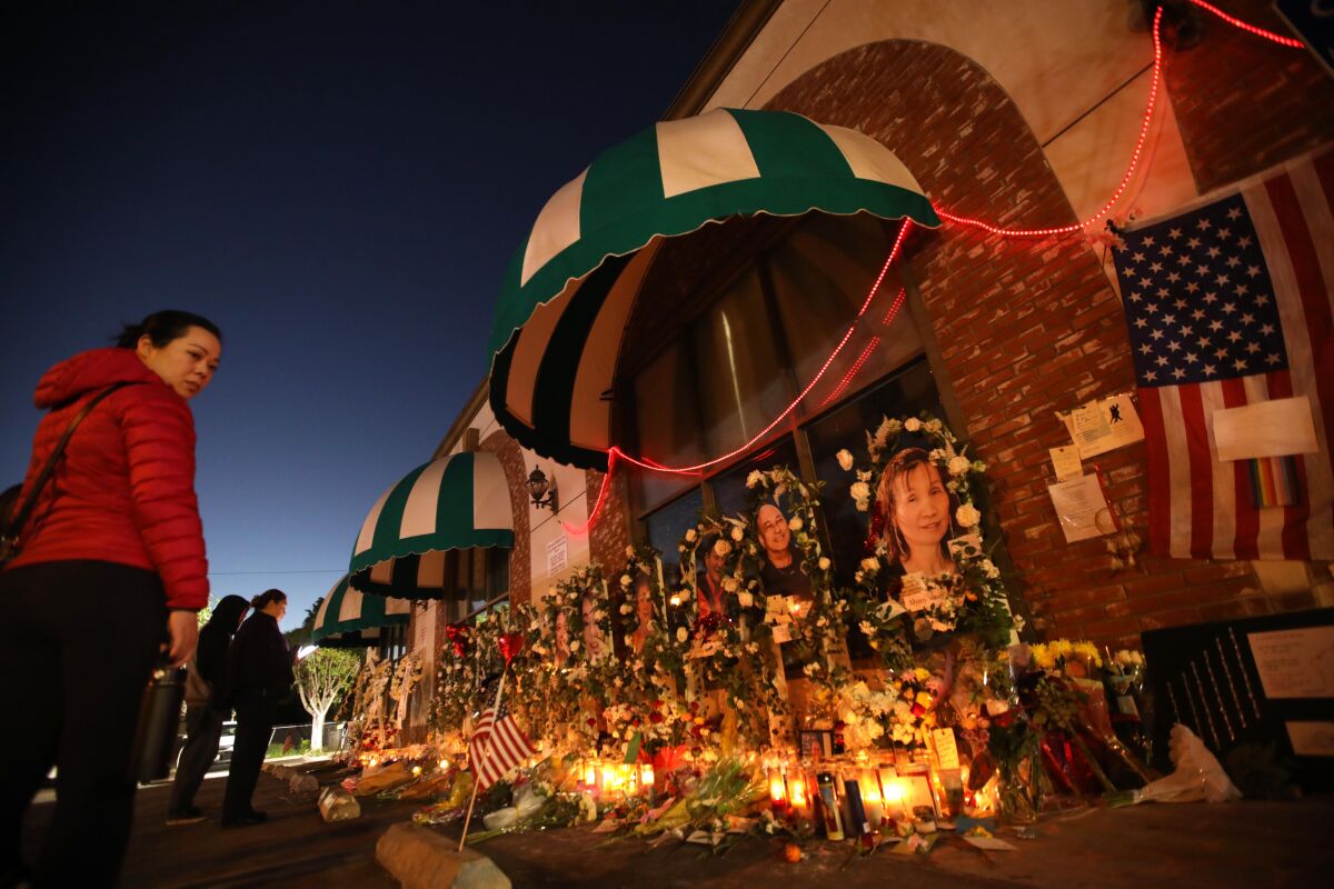 At dusk, people look at candles and flowers that fill a space alongside a business.