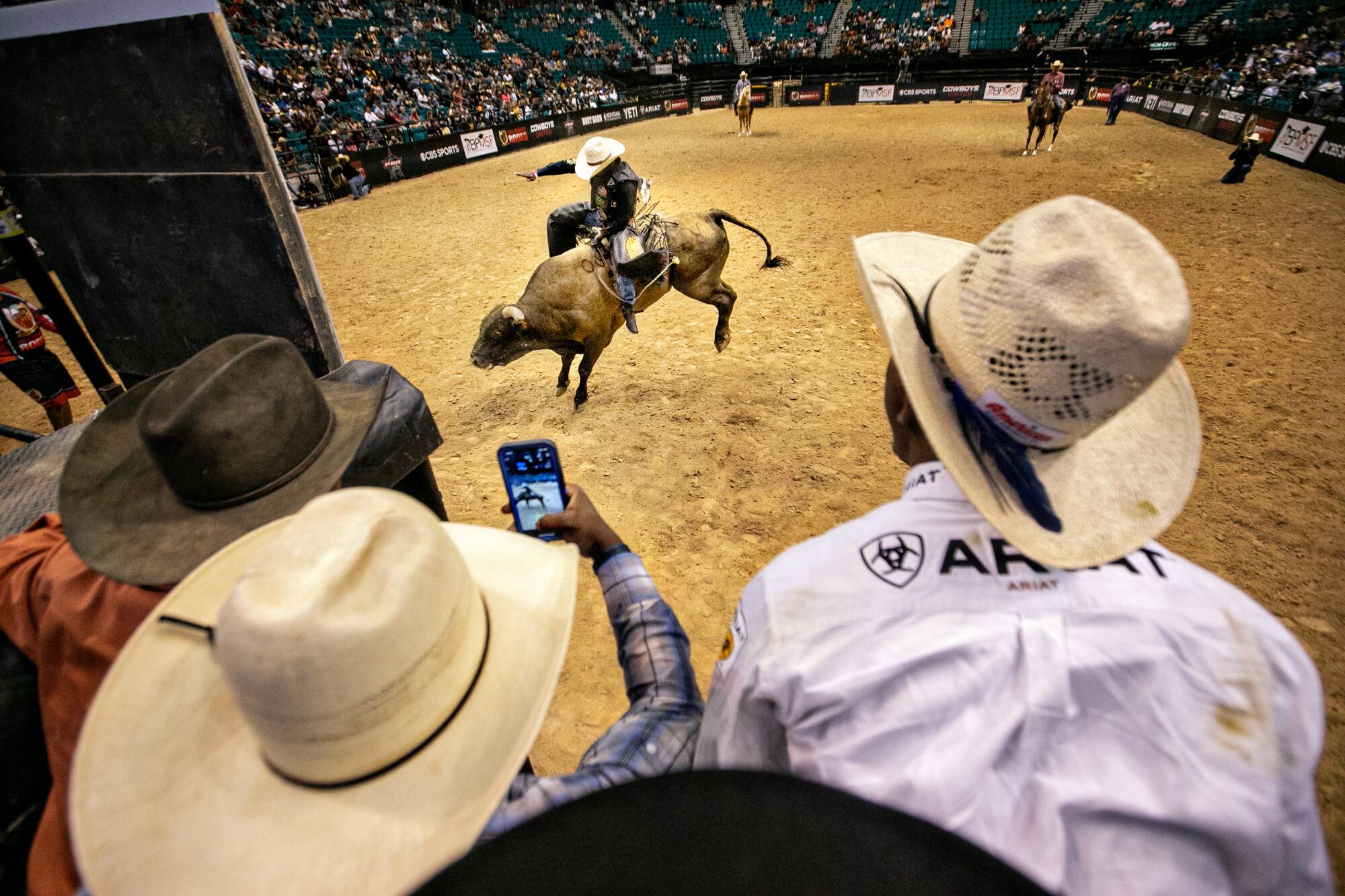 A view over the shoulders of cowboys perched on a bull-riding chute watching a competitor