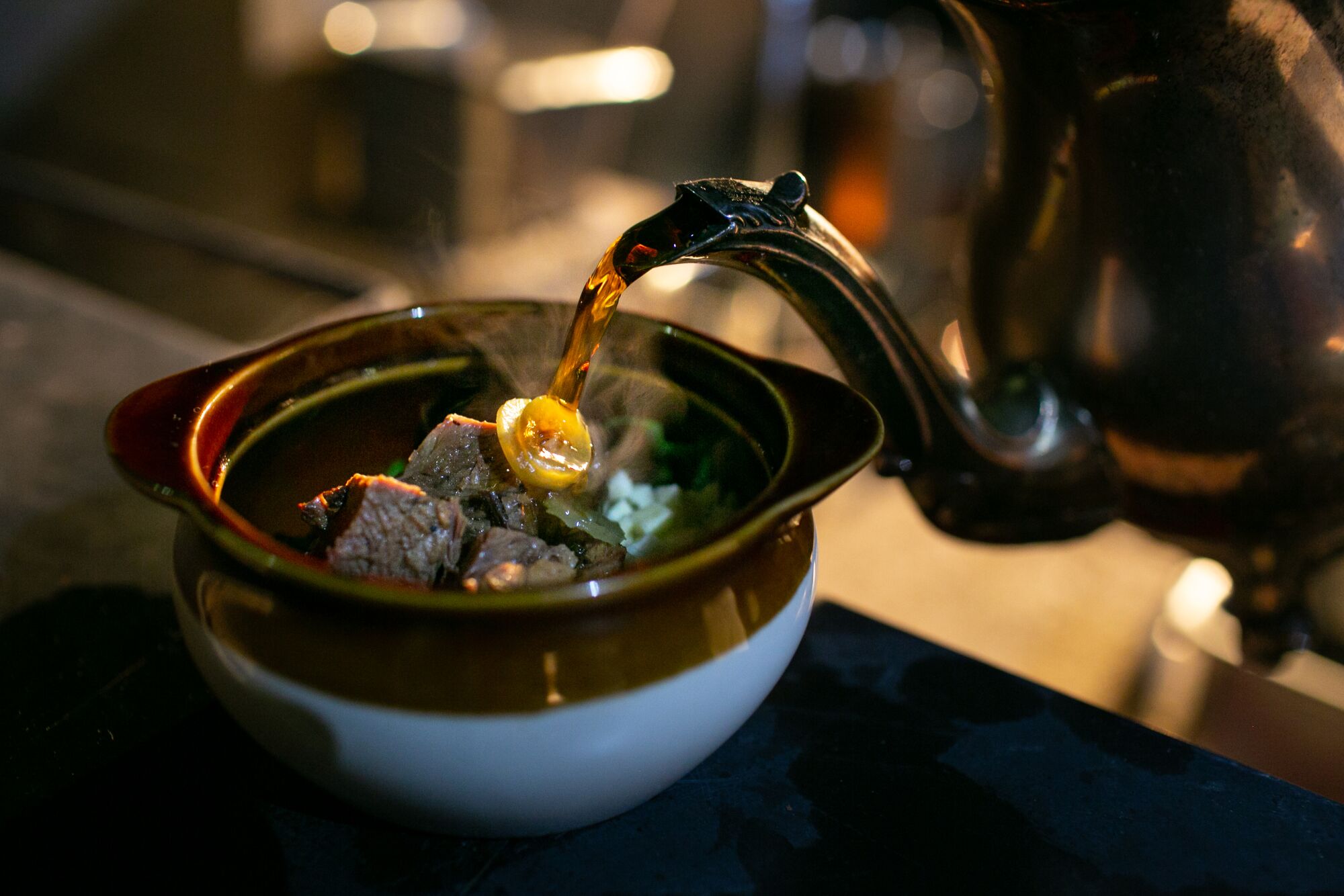 Beef broth is poured into a bowl of pepper pot, a stew made of beef, vegetables and peppers.