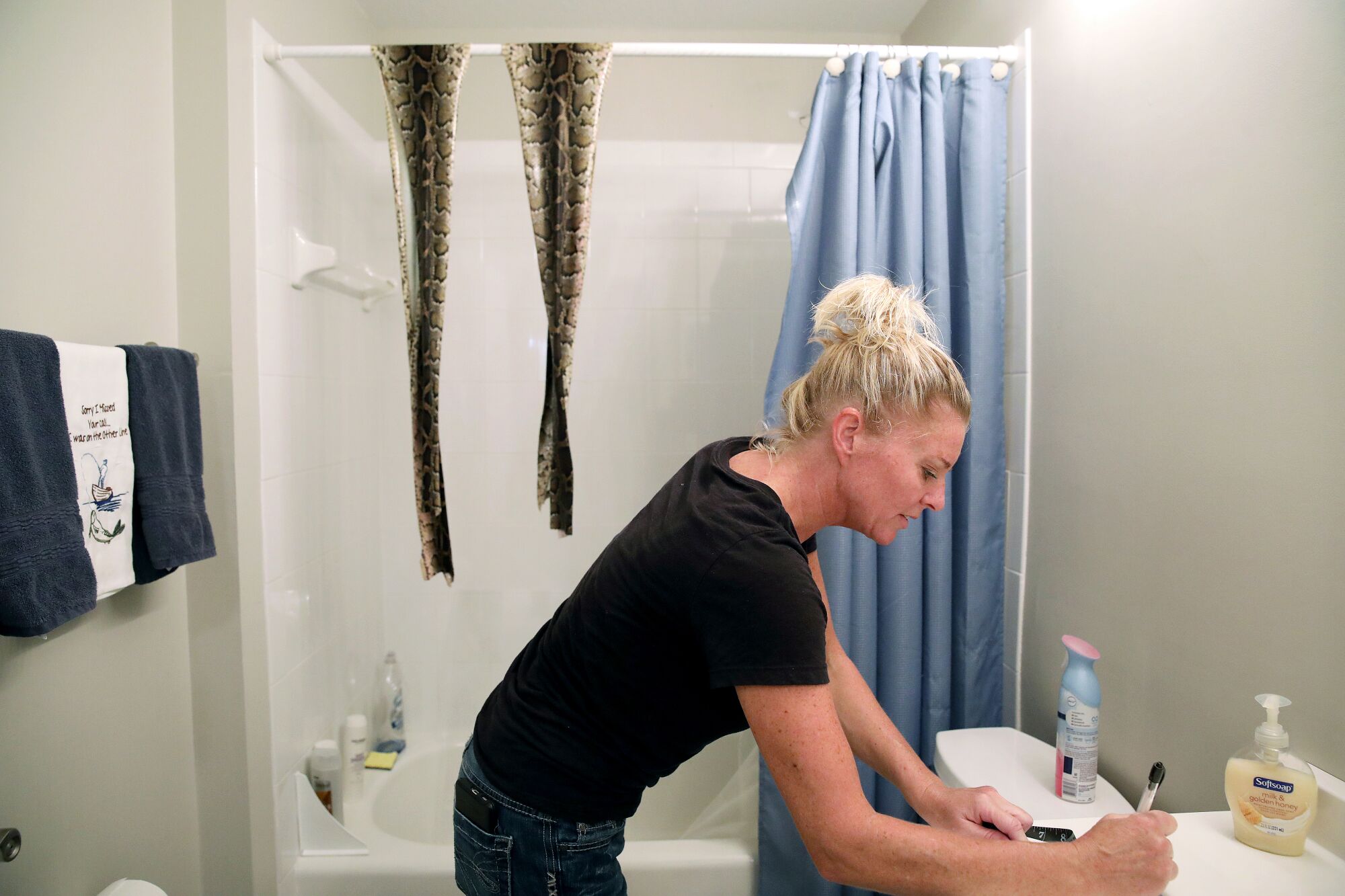 A woman documents the lengths of two python skins hanging to dry.