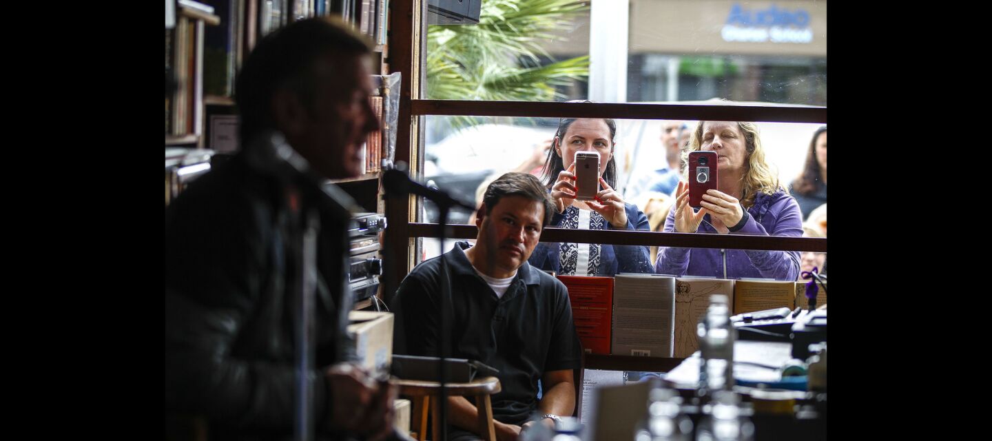 Two women take photos through a window as actor Sean Penn, foreground left, speaks into a microphone as he talks about his book 'Bob Honey Who Just Do Stuff'.