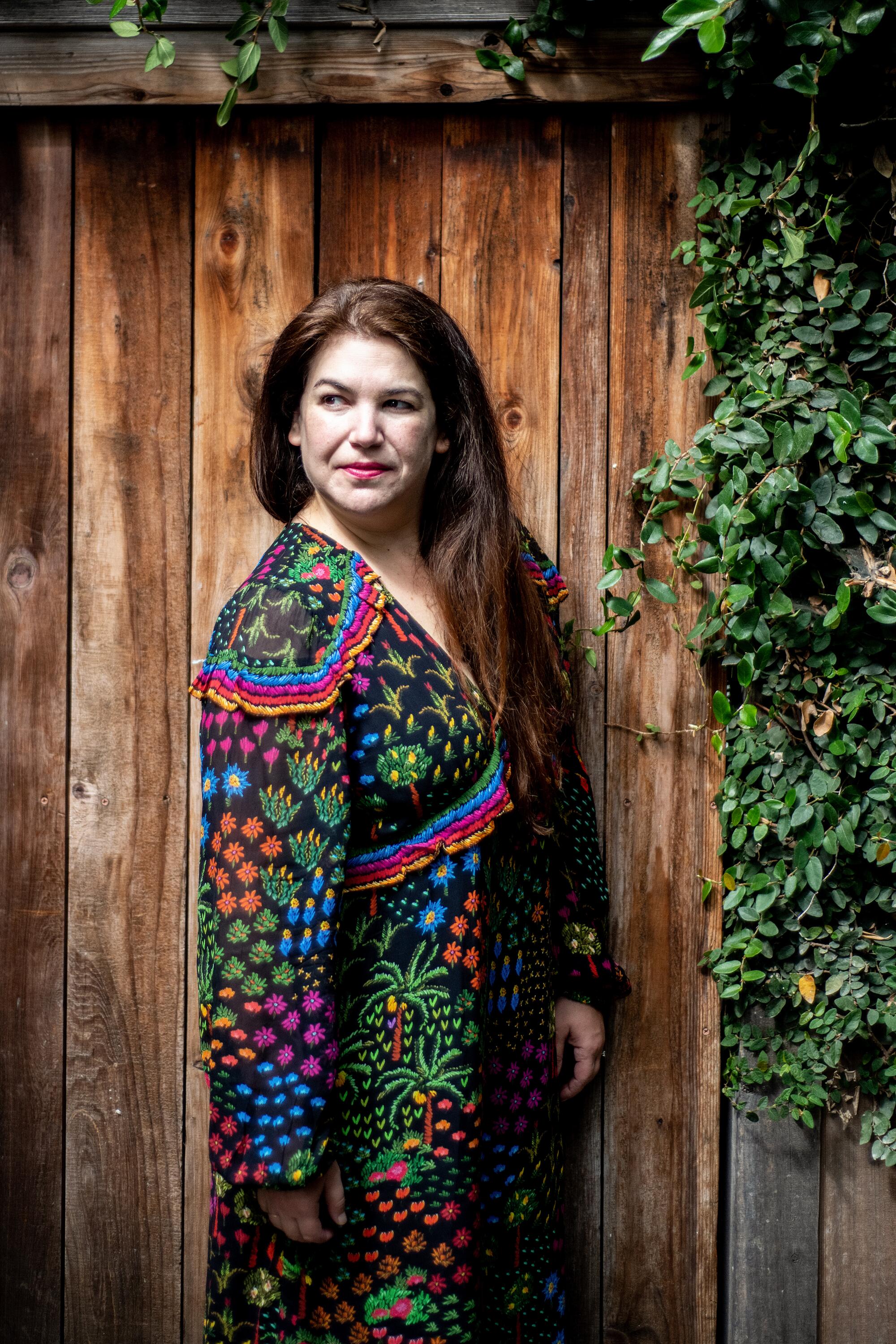  Suzanne Joskow standing in front of a wooden fence with ivy to the right.