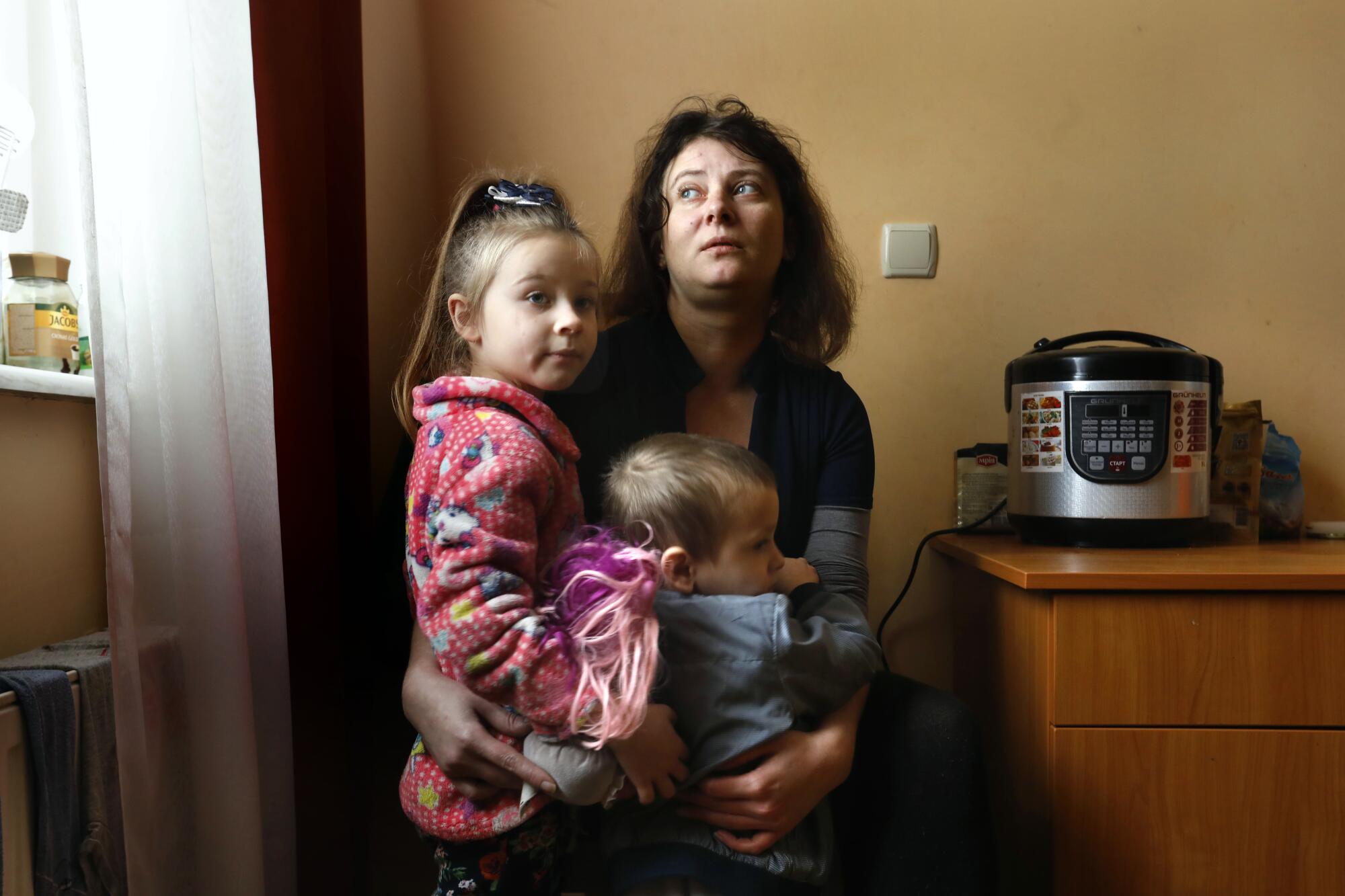 Mother holds her two children while looking out a window.