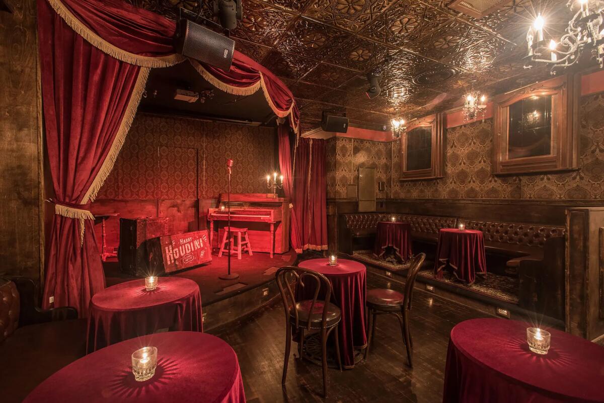 An intimate theater with tables in front of a stage with red curtains and a suitcase that reads "Harry Houdini."