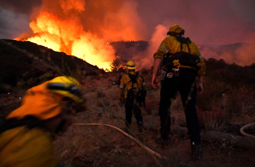 Firefighters make their way up a hill with flames ahead
