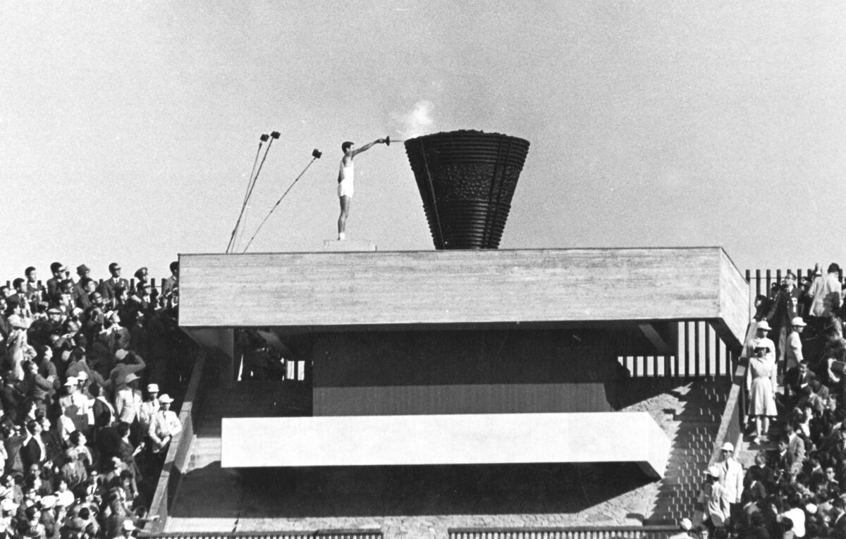 FILE - In this Oct. 10, 1964 file photo, Japanese runner Yoshinori Sakai lights the Olympic cauldron during the opening ceremony of the 1964 Summer Olympics in Tokyo. Sakai was born in Hiroshima on Aug. 6, 1945, the day the nuclear weapon destroyed that city. He symbolized the rebirth of Japan after the Second World War as he opened the 1964 Tokyo Games. Sakai was born in Hiroshima on Aug. 6, 1945, the day the United States dropped an atomic bomb on the city. Just over 19 years later, he ran with the Olympic flame into the national stadium, left the cinder track, and jogged up a long flight of flower-lined stairs to reach the top. (AP Photo/File)