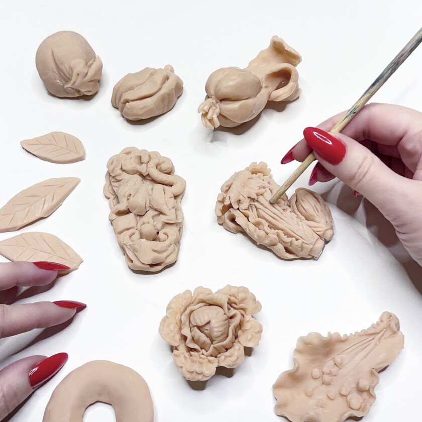 A photograph of Zilberman's hand, with bright red nails, carving the delicate molds for the edible jewelry.