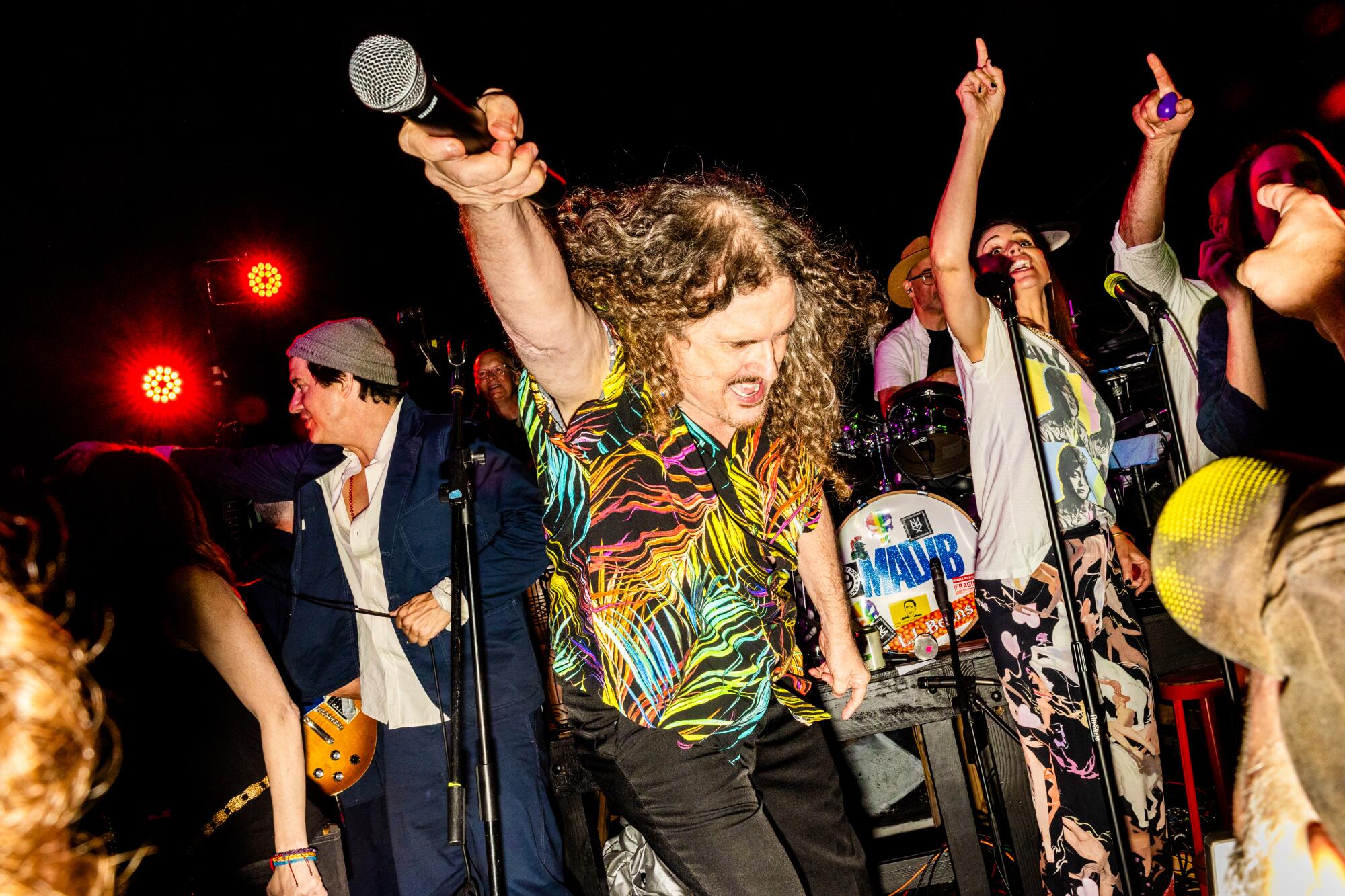 A man wearing a multicolored shirt points a microphone toward the crowd.