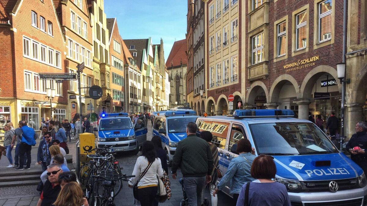 People walk past police cars in Muenster, Germany, where several people were killed or injured when a car crashed into pedestrians on Saturday, April 7, 2018.