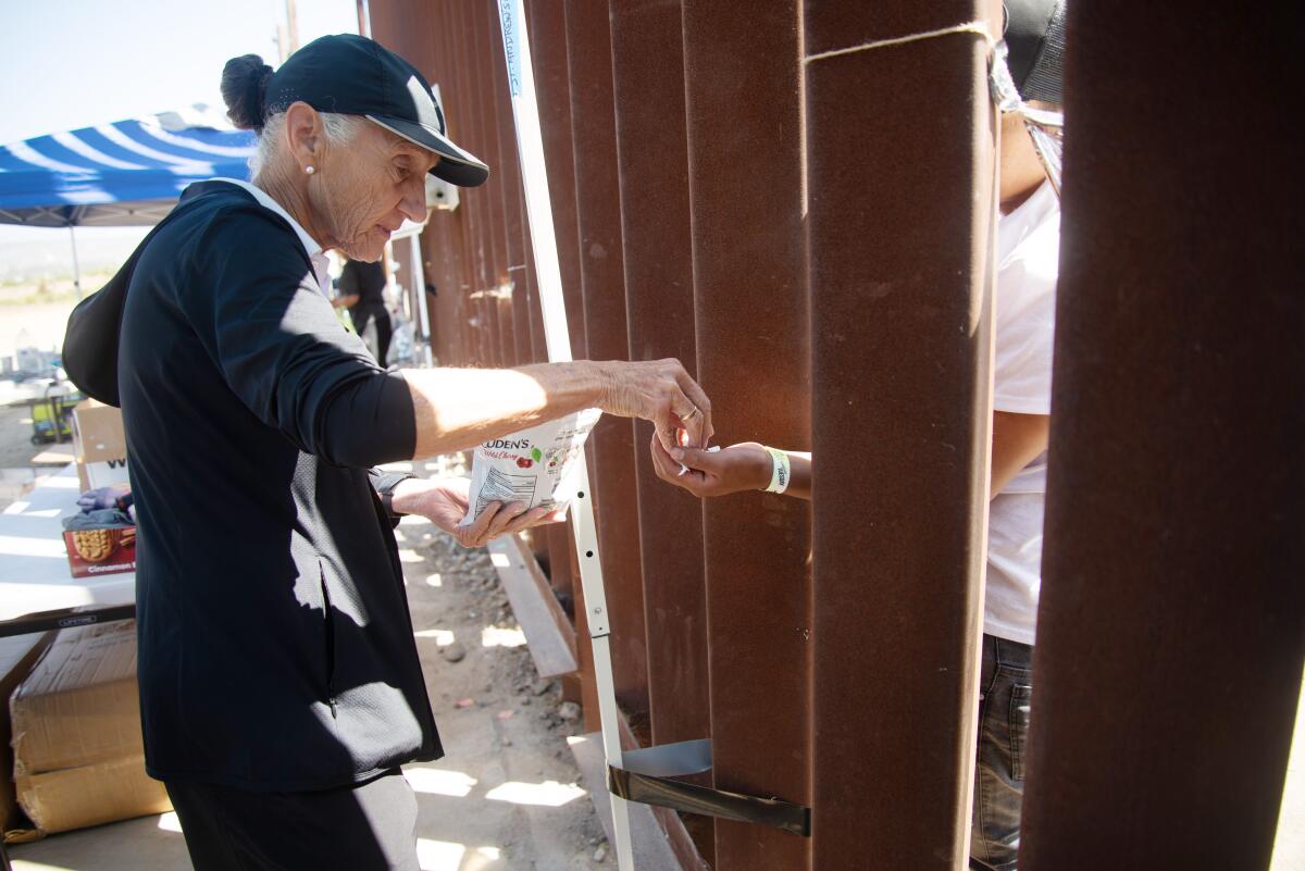 A woman hands small items to another person through bars in a metal fence.