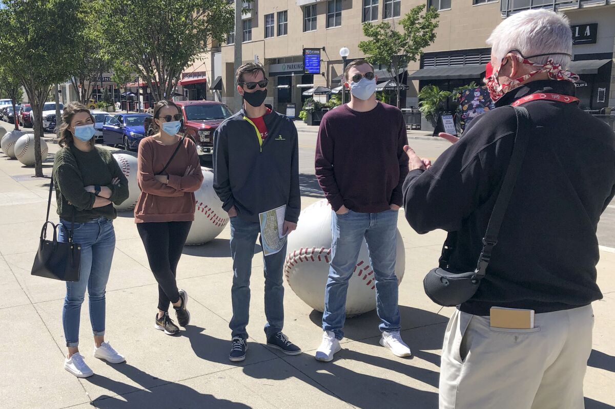 In this Sept. 20, 2020, photo, tour guide John Erardi, right, talks with a tour group on the sidewalk outside the Cincinnati Reds Great American Ball Park in Cincinnati. The walking tour was one of the few groups of people on the street as the Reds and White Sox were inside just an hour before the game without fans because of the pandemic. (AP Photo/Dan Sewell)