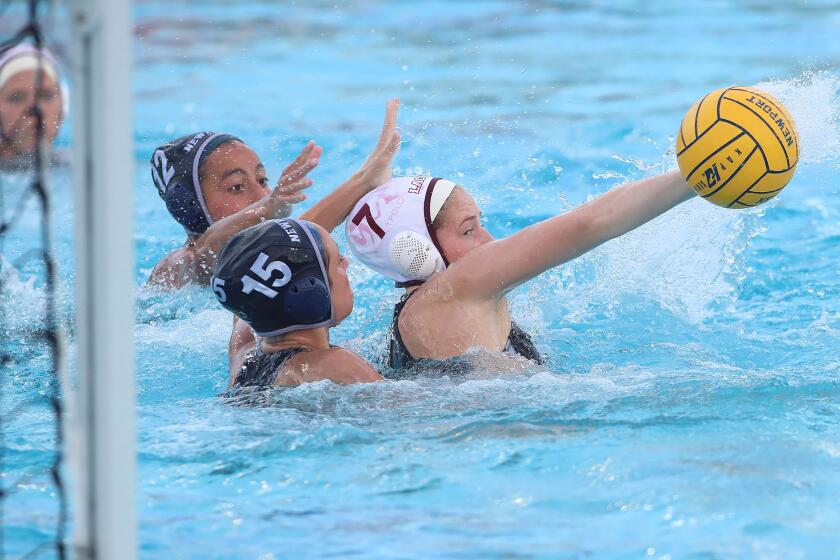 Laguna's Kara Carver shoots a behind the back shot for a score around Newport Harbor's Kylie Robison during key Surf League girls' water polo game on Tuesday.