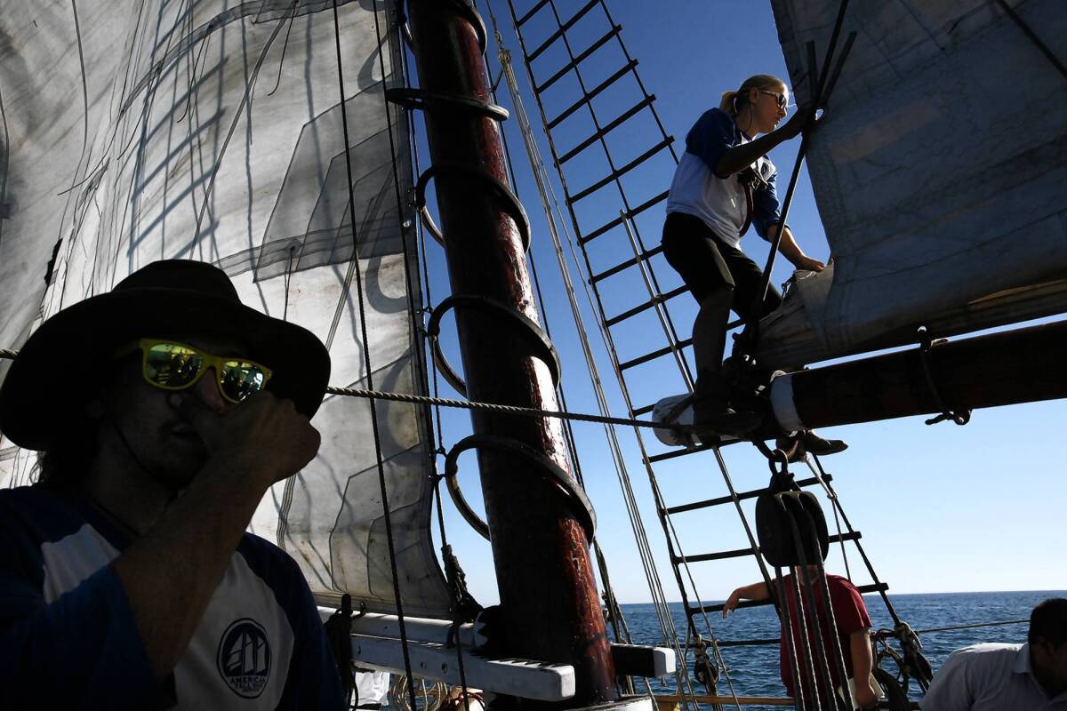 Zac Butko shouts orders as Donna Reed straddles a boom to help fold and stow a sail on the Bill of Rights. She joined the crew after giving up a real estate career and becoming stranded while biking across Europe.