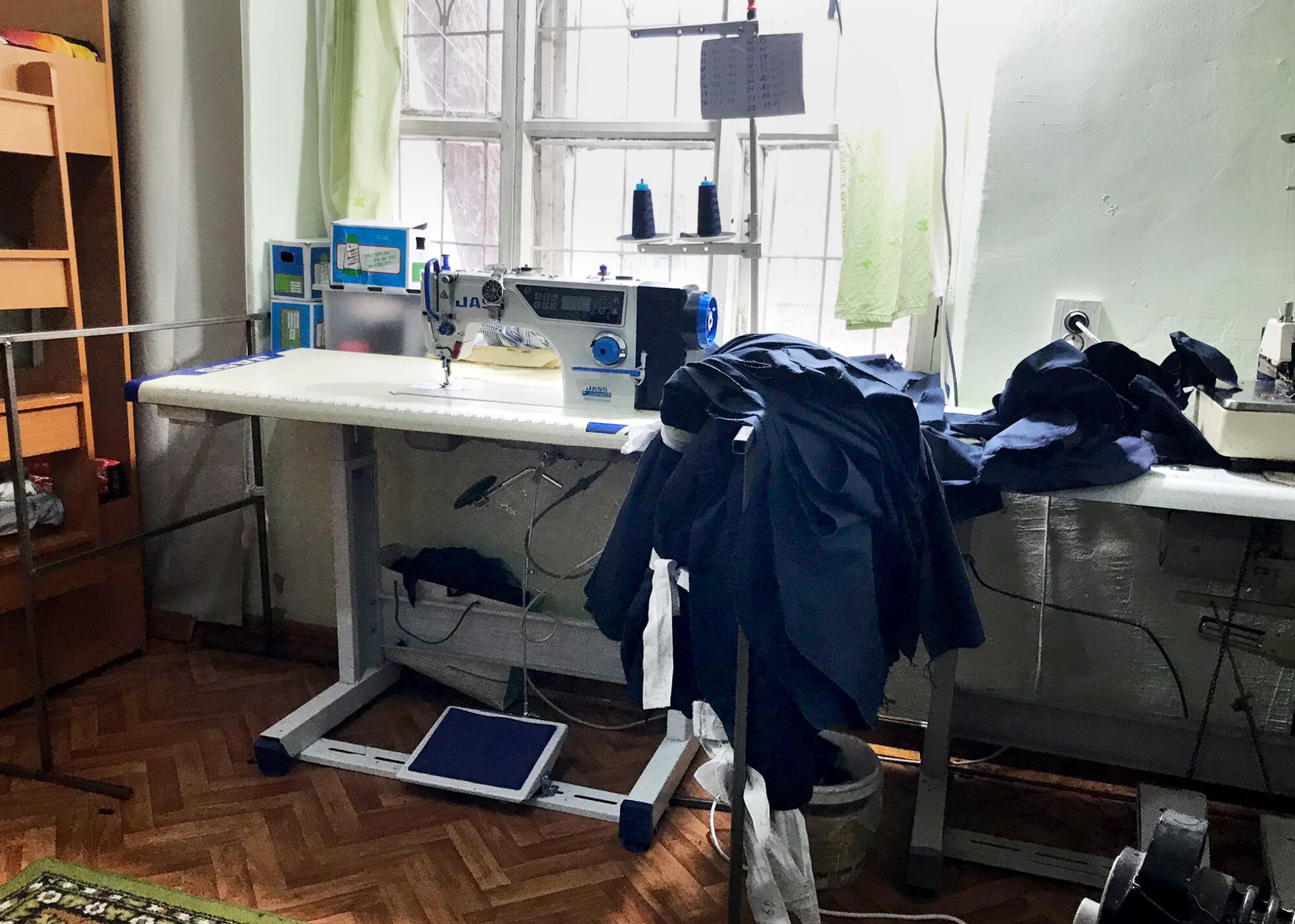 A still life of a sewing machine set up near a window. Nearby is a pile of dark cloth