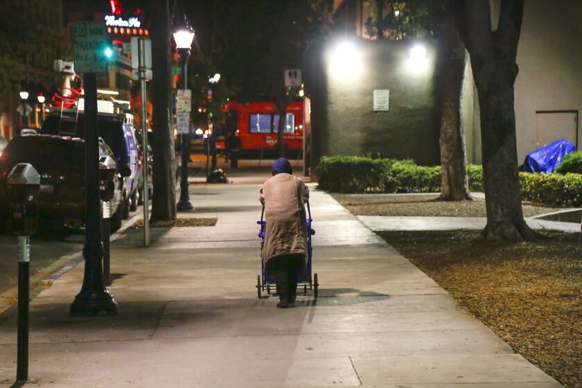 A homeless woman pushes her belongings in a cart as she walks along Third Avenue in downtown San Diego.